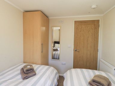 A bedroom with two single beds towels on beds a wooden wardrobe a wall mirror and a wooden door at Horseshoe Lodge Wansfell 5 Limefitt Park near Windermere