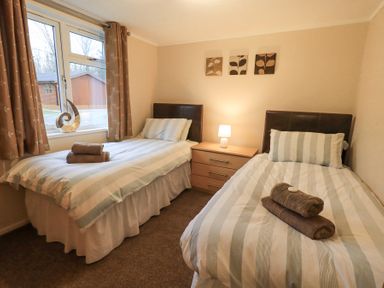 A bedroom with two single beds a bedside table with lamp and window with curtains at Horseshoe Lodge Wansfell 5 Limefitt Park near Windermere
