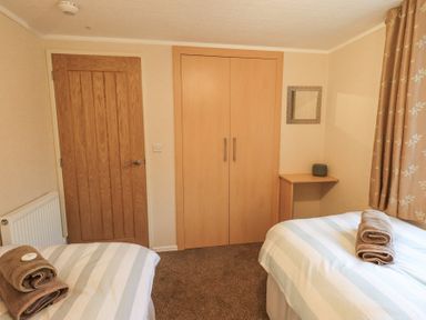 A bedroom with two single beds with folded towels a wooden door a built-in wardrobe and a small corner shelf at Horseshoe Lodge Wansfell 5 Limefitt Park near Windermere