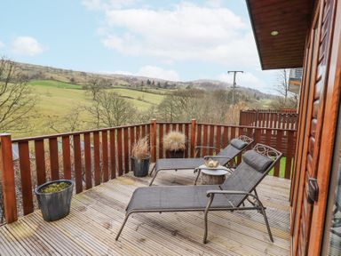 A wooden balcony with two lounge chairs a small table and potted plants overlooking green hills and trees at Horseshoe Lodge in Wansfell 5 Limefitt Park near Windermere