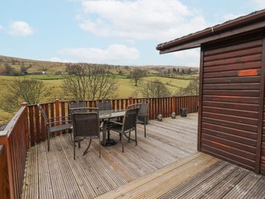An outdoor wooden deck with a table and six chairs overlooking fields and hills at Horseshoe Lodge Wansfell 5 Limefitt Park near Windermere