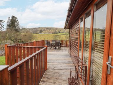 A wooden balcony with a table and chairs overlooking fields and hills at Horseshoe Lodge Wansfell 5 Limefitt Park near Windermere