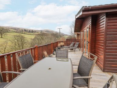 A wooden deck with outdoor dining table and chairs overlooking grassy hills at Horseshoe Lodge Wansfell 5 Limefitt Park near Windermere