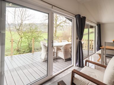 A dining area with sliding glass doors opening to a deck with outdoor chairs and table at Jinnyspinner Lodge Beckside 37 Limefitt Park near Windermere
