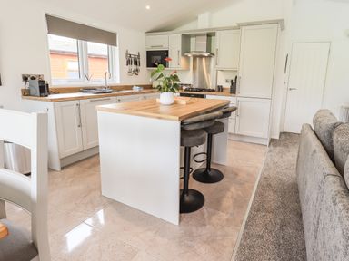 A kitchen with an island and bar stools with a couch nearby at Jinnyspinner Lodge Beckside 37 Limefitt Park near Windermere
