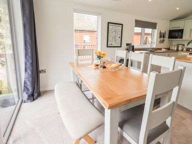 A dining table with chairs and a bench in a kitchen with windows and kitchen appliances at Jinnyspinner Lodge Beckside 37 Limefitt Park near Windermere
