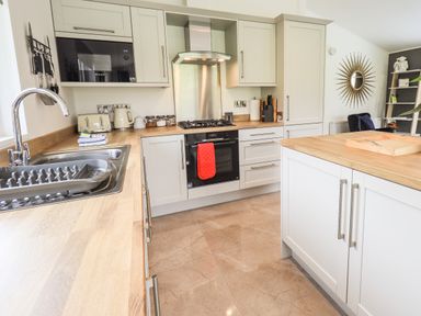 A kitchen with a wooden countertop sink oven microwave and a red oven glove at Jinnyspinner Lodge Beckside 37 Limefitt Park near Windermere