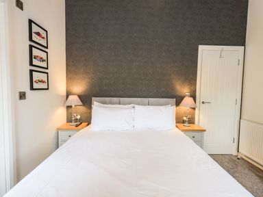 A bedroom with a double bed two bedside tables with lamps a door and three framed pictures on the wall at Jinnyspinner Lodge Beckside 37 Limefitt Park near Windermere