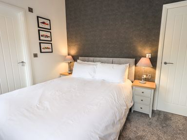 A bedroom with a bed, two bedside tables, lamps, three framed pictures, and two doors at Jinnyspinner Lodge Beckside 37 Limefitt Park near Windermere