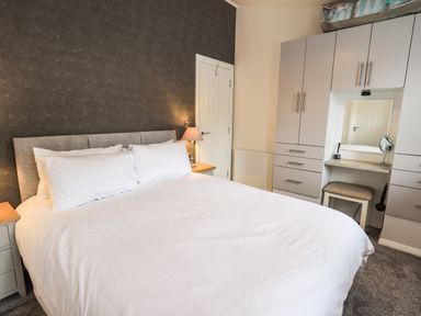 A bedroom with a large bed bedside tables a lamp and a built in wardrobe with a dressing table at Jinnyspinner Lodge Beckside 37 Limefitt Park near Windermere