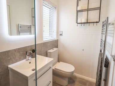 A bathroom with a sink vanity mirror toilet window and wall shelf at Jinnyspinner Lodge Beckside 37 Limefitt Park near Windermere