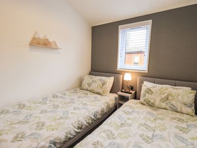A bedroom with two single beds a nightstand with a lamp and a window at Jinnyspinner Lodge Beckside 37 Limefitt Park near Windermere