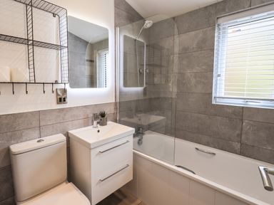 A bathroom with a toilet sink with vanity mirror bathtub and window with blinds at Jinnyspinner Lodge Beckside 37 Limefitt Park near Windermere