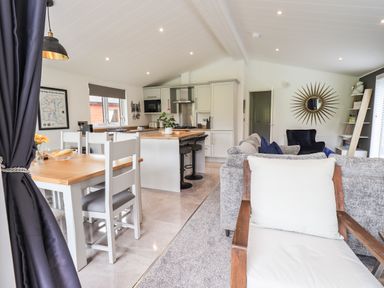 An open plan kitchen and living area with dining table chairs kitchen island and sofa at Jinnyspinner Lodge Beckside 37 Limefitt Park near Windermere