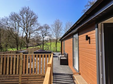 An outdoor wooden deck with seating and railing beside a wooden building with windows and door at Jinnyspinner Lodge Beckside 37 Limefitt Park near Windermere