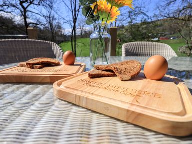 A glass table outdoors with wooden chopping boards holding boiled eggs and bread slices with a vase of sunflowers on the table at Jinnyspinner Lodge Beckside 37 Limefitt Park near Windermere