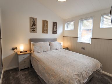 A bedroom with a double bed nightstands with lamps and three framed artworks above the bed at Jinnyspinner Lodge Beckside 37 Limefitt Park near Windermere