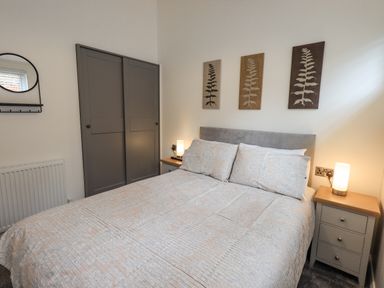 A bedroom with a bed a bedside table with a lamp a wardrobe and three framed plant prints on the wall at Jinnyspinner Lodge Beckside 37 Limefitt Park near Windermere