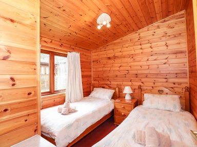 A bedroom with two single beds wooden walls and a window at Rowan Lodge Pinewood 16 Limefitt Park near Windermere