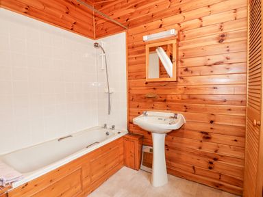 A bathroom with a bathtub shower sink mirror and wooden walls at Rowan Lodge Pinewood 16 Limefitt Park near Windermere
