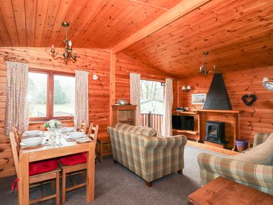 A living room with a dining table set for six people and two plaid sofas next to a fireplace at Rowan Lodge in Pinewood 16 Limefitt Park near Windermere