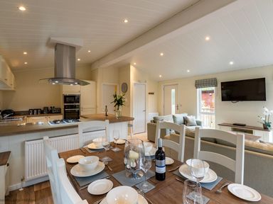 A dining table set with plates glasses and a bottle of wine in an open plan kitchen and living area at Langdale Lodge Langdale 21 White Cross Bay near Windermere