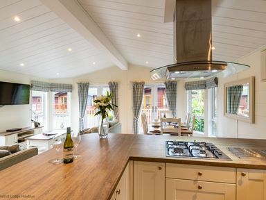 A kitchen with a wooden countertop and gas stove overlooking a dining area and living room with windows at Langdale Lodge Langdale 21 White Cross Bay near Windermere