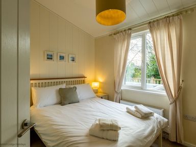 A bedroom with a double bed two bedside tables with lamps a window with curtains and folded towels on the bed at Langdale Lodge Langdale 21 White Cross Bay near Windermere
