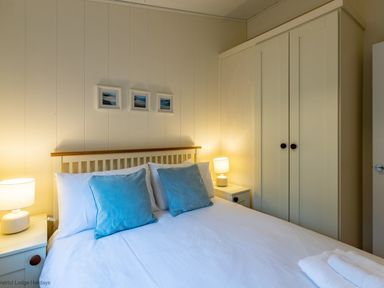 A bedroom with a double bed with blue pillows two bedside tables with lamps and a wardrobe at Langdale Lodge Langdale 21 White Cross Bay near Windermere