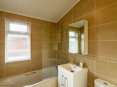 A bathroom with a bathtub shower combination a white sink with mirror above and a toilet at Langdale Lodge in Langdale 21 White Cross Bay near Windermere