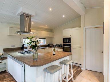 A kitchen with wooden countertops stools in front a stove and a vase of flowers at Langdale Lodge Langdale 21 White Cross Bay near Windermere