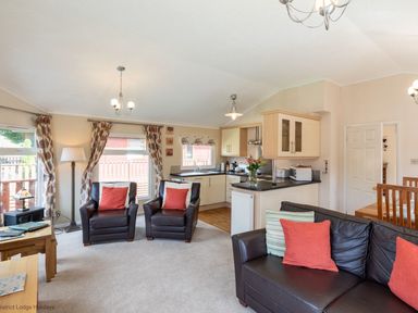 A living room with brown leather chairs and a sofa with cushions near a kitchen with light wood cabinets at Hideaway Lodge Kirkstone 14 Limefitt Park near Windermere