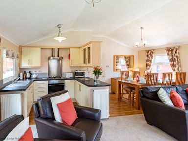 An open kitchen with cream cabinets a dining table set with chairs and a living area with leather sofas at Hideaway Lodge Kirkstone 14 Limefitt Park near Windermere