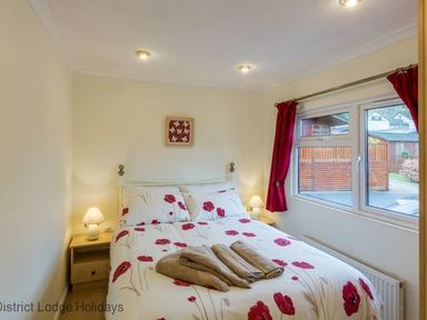 A bedroom with a double bed and floral bedding beside a window with red curtains at Hideaway Lodge Kirkstone 14 Limefitt Park near Windermere