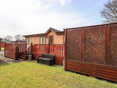 An outdoor view of a wooden lodge with railing and steps a bench and lattice fences at Valley View Lodge in Wansfell 10 Limefitt Park near Windermere