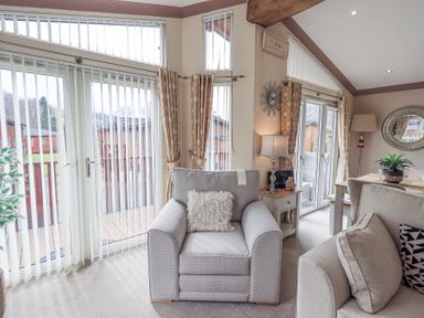A living room with an armchair a sofa a table lamp and vertical blinds at Valley View Lodge Wansfell 10 Limefitt Park near Windermere