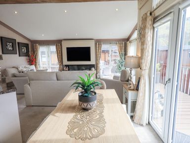 A living room with sofas a television a plant on a wooden table and large windows at Valley View Lodge Wansfell 10 Limefitt Park near Windermere
