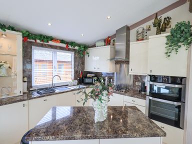 A kitchen with white cabinets a window above the sink and a countertop island with flowers at Valley View Lodge Wansfell 10 Limefitt Park near Windermere
