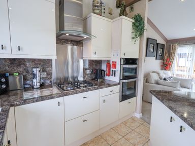 A kitchen with a gas stove oven and white cabinets next to a living area with a sofa at Valley View Lodge Wansfell 10 Limefitt Park near Windermere