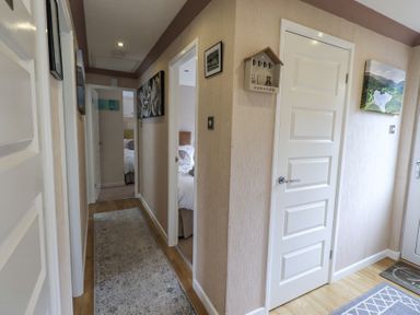 A hallway with a beige runner rug leading to multiple white doors and two bedrooms visible at Valley View Lodge in Wansfell 10 Limefitt Park near Windermere