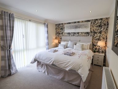 A bedroom with a large bed bedside tables lamps and floral wallpaper at Valley View Lodge Wansfell 10 Limefitt Park near Windermere