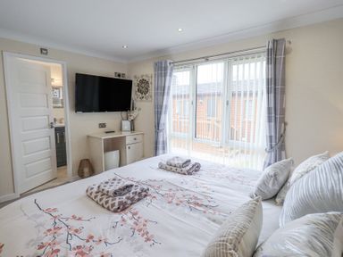 A bedroom with a bed facing a wall-mounted TV and window with curtains at Valley View Lodge Wansfell 10 Limefitt Park near Windermere