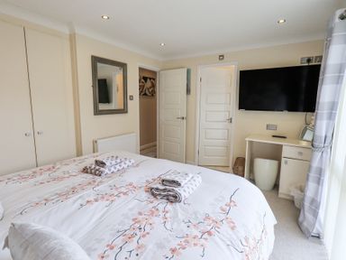 A bedroom with a bed, folded towels, a wall mirror, and a TV mounted above a desk at Valley View Lodge Wansfell 10 Limefitt Park near Windermere