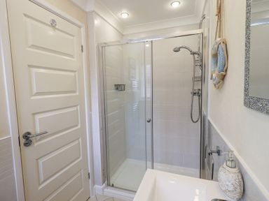 A bathroom with a glass shower enclosure a cream door a sink with soap dispenser and a decorative wall mirror at Valley View Lodge Wansfell 10 Limefitt Park near Windermere