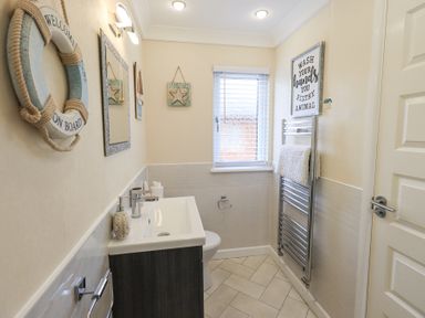A bathroom with a sink, a mirror, a window with blinds, a towel rack, and wall decorations at Valley View Lodge Wansfell 10 Limefitt Park near Windermere