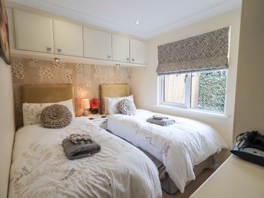 A bedroom with two single beds a window with blinds and overhead cabinets at Valley View Lodge Wansfell 10 Limefitt Park near Windermere