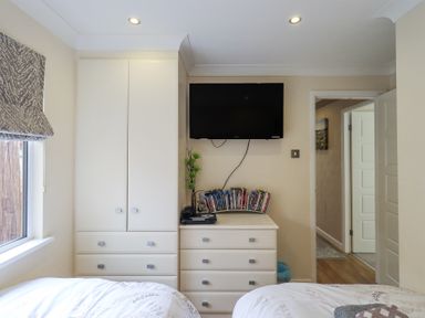 A bedroom with two beds a chest of drawers a wardrobe a TV on the wall and a window with a patterned blind at Valley View Lodge Wansfell 10 Limefitt Park near Windermere