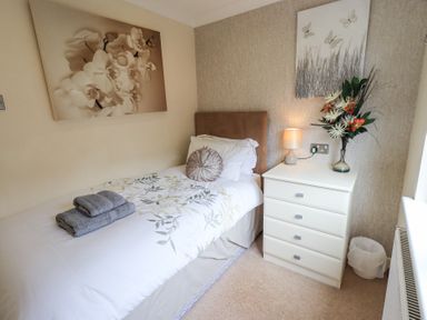 A bedroom with a single bed a chest of drawers a lamp and a vase with flowers at Valley View Lodge Wansfell 10 Limefitt Park near Windermere
