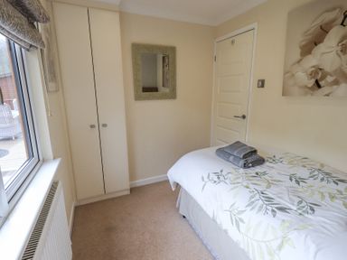 A bedroom with a single bed a folded towels on the bed a mirror on the wall and a window at Valley View Lodge Wansfell 10 Limefitt Park near Windermere
