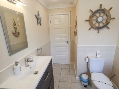A bathroom with a sink and mirror on the left and a toilet with nautical decorations on the right at Valley View Lodge Wansfell 10 Limefitt Park near Windermere